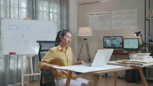 Asian Woman Engineer Walk Into The Office Before Looking At Blueprint And Typing On A Laptop