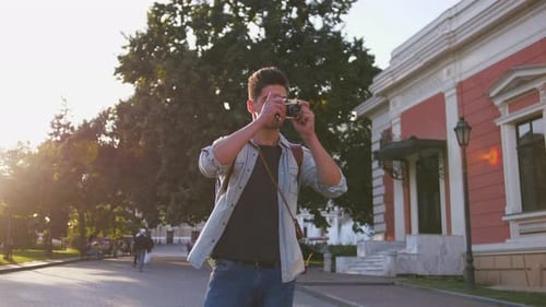 Young Attractive Handsome Man Tourist with Backpack Taking Photos on Vintage Camera in Old City
