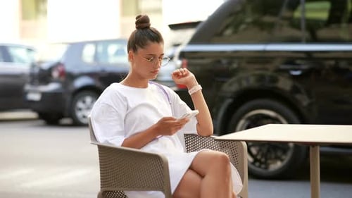 Beautiful Young Woman Sitting in Street Cafe Using a Smartphone