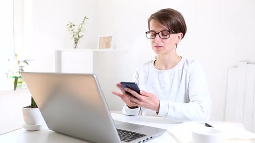 A woman sitting at home works at a computer. Freelancer works remotely at a laptop.