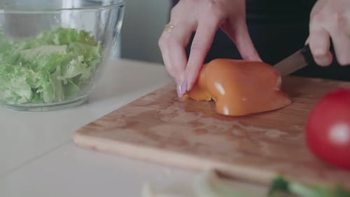 Weibliche Hände schneiden roten Pfeffer für Salat in der Küche