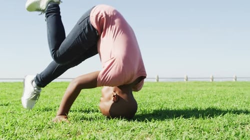 Video of happy african american boy doing rolls on meadow