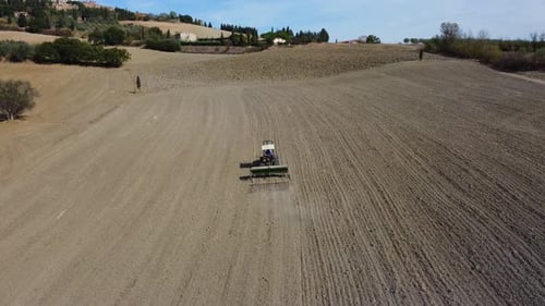Tractor plowing ground soil in rural agriculture wheat field aerial view in Pienza, Tuscany