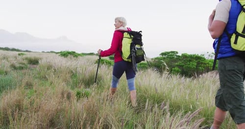 Couple Hiking Through Grassy Field on a Cloudy Day