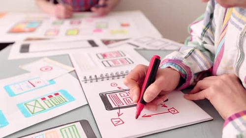 Designer Drawing Mobile App Interface Diagrams in Notebook