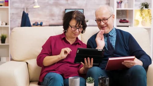 Senior Couple Relaxing with Tablet and Book at Home