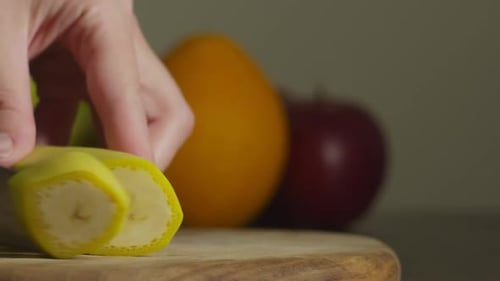 Closeup of Hand Holding Kitchen Knife Cutting Banana Indoors