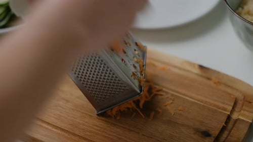 Nahaufnahme weiblicher Hände, die Karotten auf einem weißen Tisch reiben. Ansicht von oben Salat kochen.