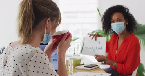 Woman wearing face mask showing a document to her colleague at office