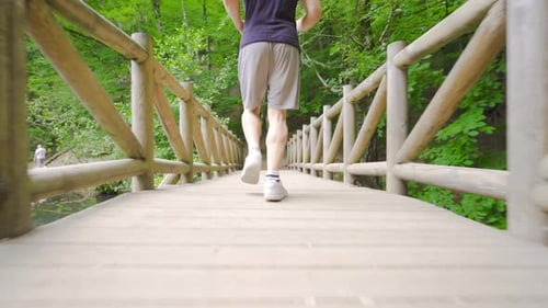 Man Running Across a Wooden Bridge in Nature