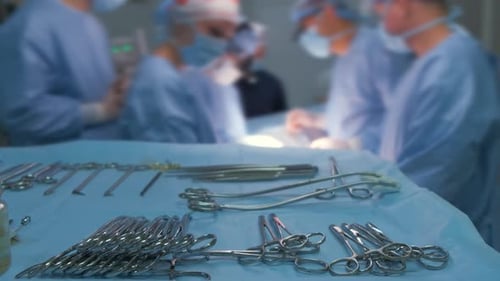Closeup of Surgical Tools on Table and Team of Surgery Doctors Operating a Patient in Hospital Room