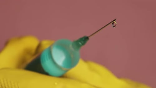 Spritzennadel mit Flüssigkeit tropfenden Medikamententropfen in die Hände des Arztes