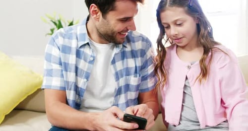 Father and Daughter Smiling Together While Using Smartphone