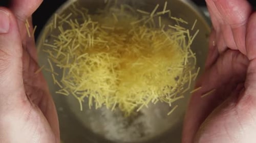 Hands Pouring Vermicelli Pasta Into Boiling Water