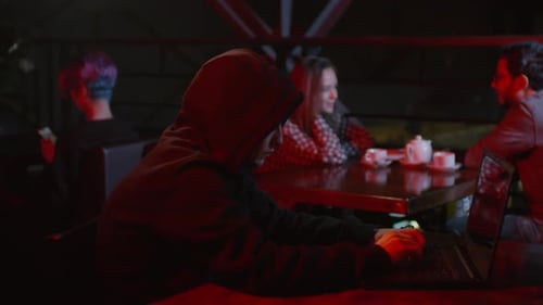 Hooded Hacker Sitting at PC in Bar