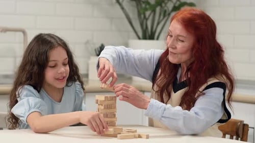 Grandmother and Granddaughter Play a Board Game at Home Build a Tower From Wooden Blocks