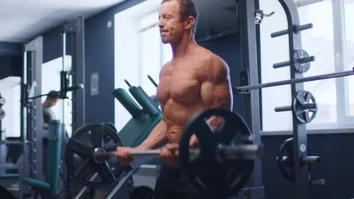 Älterer männlicher Athlet macht Langhantel-Curl-Übungen in einem Fitnessstudio