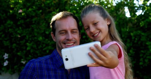 Father and daughter taking selfie on mobile phone in park