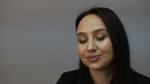 Brunette european woman looking at camera while standing in the office on gray background