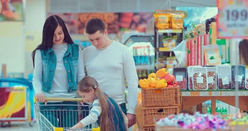 Father Mother and Little Daughter Picking Peanuts in a Package in a Supermarket