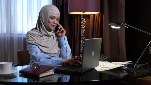Woman Talking on Phone While Typing on Laptop