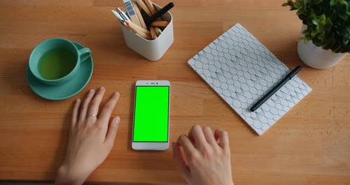 Close-up of Female Hand Touching Green Chroma-key Smartphone Screen on Table