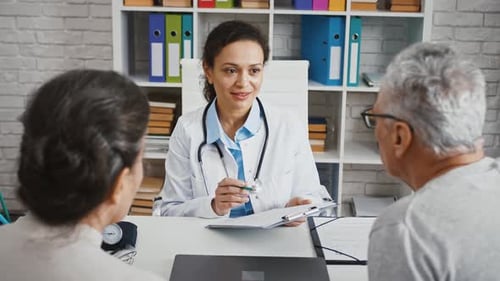 Doctor Woman Consulting Aged Patients Sitting at Table in Cabinet of Modern Clinic Explaining