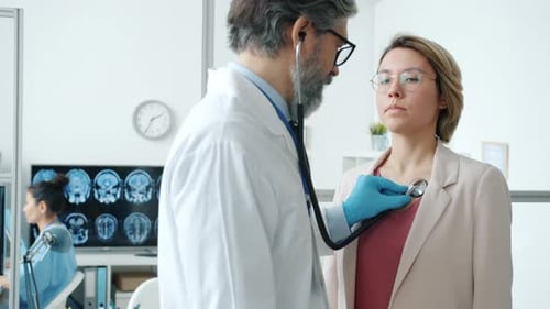 Male Doctor Using Stethoscope While Female Patient Breathing During Medical Exam in Clinic