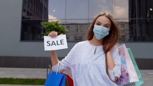 Girl in Protective Mask with Shopping Bags Showing Sale Word Inscription During Covid-19 Pandemic