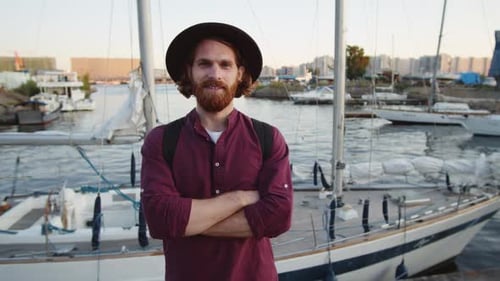 Homem de gengibre sorridente usando chapéu em pé perto da baía