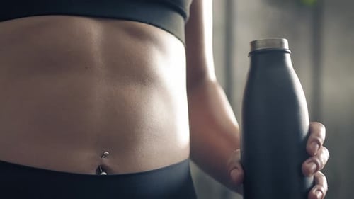 Backlit Close Up of Fitness Woman Abs While Raising Sport Bottle To Drink. Athlete Woman Abs Muscles