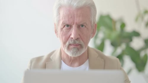 Close Up of Old Man Looking at Camera While Using Laptop in Office
