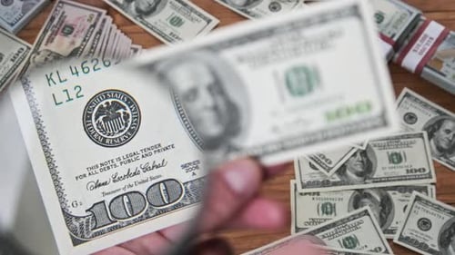 One Hundred Dollars Inspecting Under Magnifying Glass on Money Background