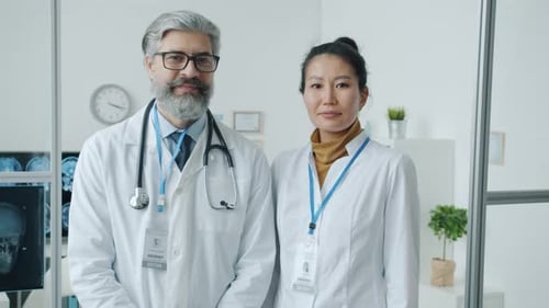 Doctors Man and Woman in White Coats Standing in Hospital Office Smiling and Looking at Camera