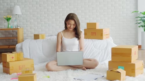 Woman Working on Laptop Surrounded by Boxes