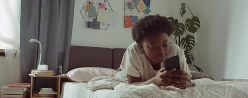 Young Adult Using Mobile Phone Lying on Bed