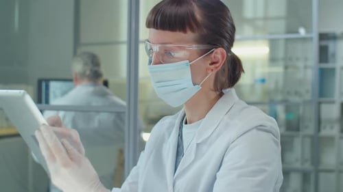 Masked Female Scientist Using Tablet in Lab
