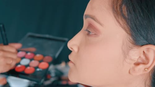 Nahaufnahme eines professionellen Maskenbildners, der das Rouge mit einem Make-up-Pinsel auf das Gesicht der Frau legt