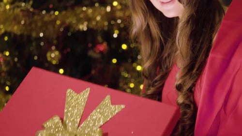 Woman Opens Gift in front of Christmas Tree