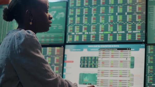 Broker femenino mirando monitores múltiples con estadísticas de cambio de divisas