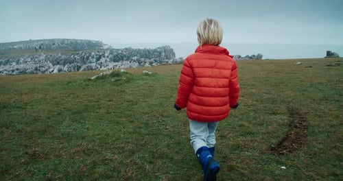Cute Happy Child Boy Walk on Green Grass to the Edge of Ocean Shore