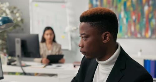 Darkskinned Man in Jacket with Colored Hair Works in Company Office Fills Out Documents on Compute