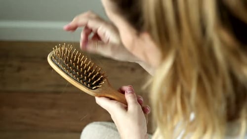 Woman Removes Hair from Wooden Hairbrush Indoors