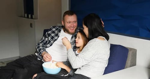 Family Eating Popcorn Together on Couch Indoors