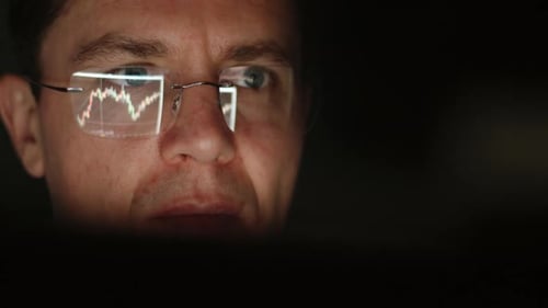 Focused Man Watches Stock Chart Reflected in Glasses