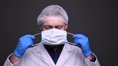 Man puts on surgical mask, looking at camera