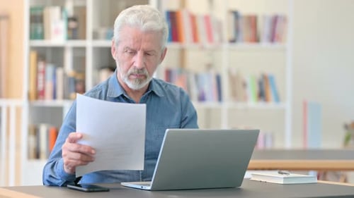 Senior Man Reviews Paperwork at Workplace Desk