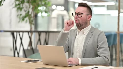 Man Coughing While Typing On Laptop in Office