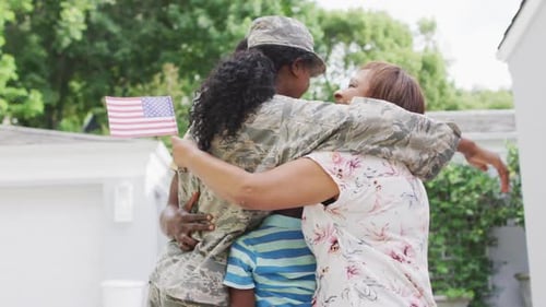 Military Woman Embraced by Family Holding American Flags