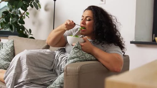 Woman Relaxes on Sofa Eating Salad